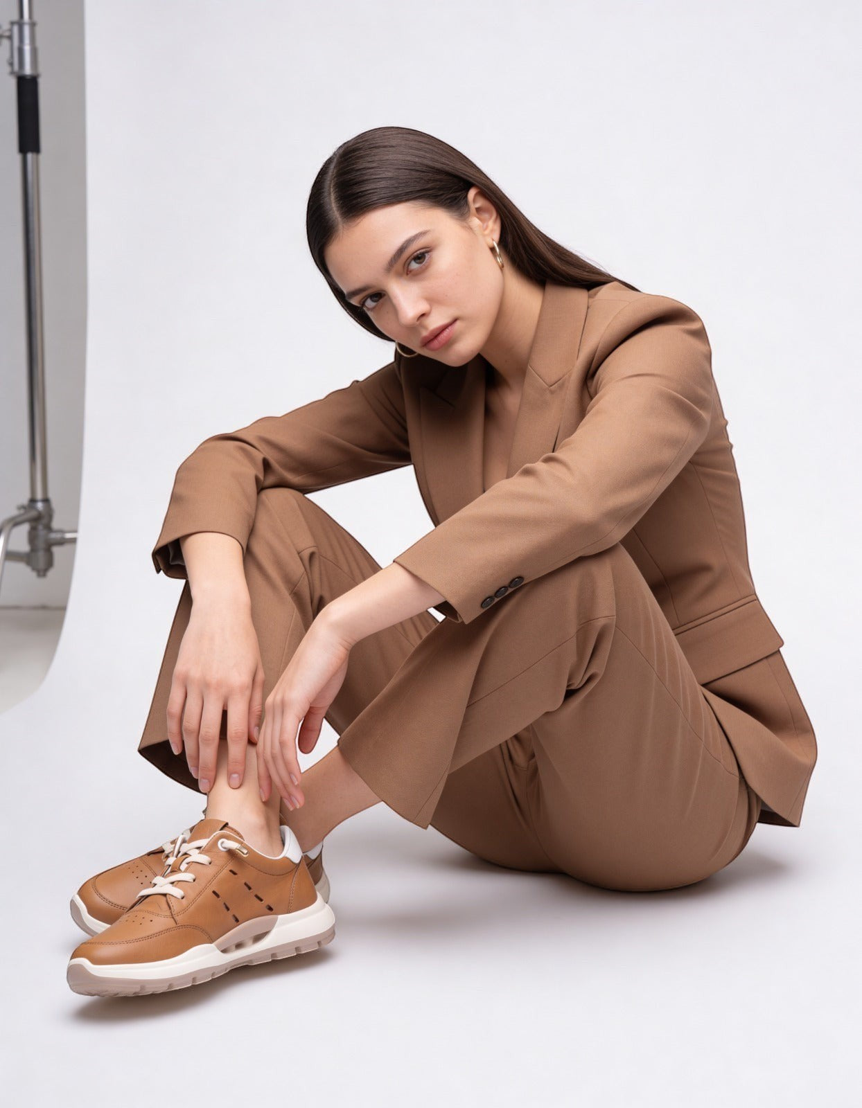 MrCalvano Comfort Walk taba rengi deri sneaker giyen, kahverengi takım elbiseli kadın model stüdyo çekimi